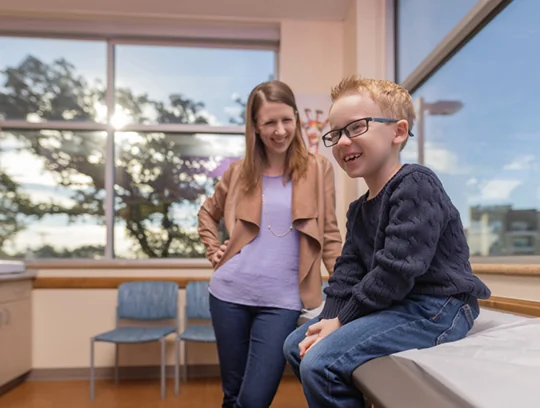 A young kid smiling in a doctor's office while his mom smiles at him