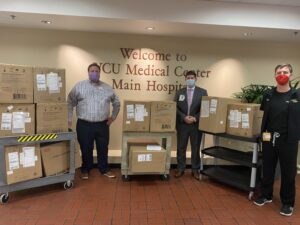 three men stand beside carts full of boxes filled with KN95 mask donations