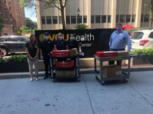 four people stand outside in front of a VCU Health banner wearing masks and with two carts full of food donated by Panda Express