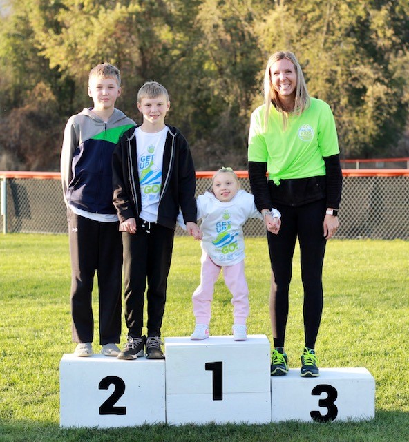 Elyse's brothers, Elyse, and mom Amanda pose on the winner's podium at the Healthy Kids Running Series