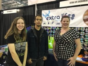 Two women and one man posing in front of an Extra Life banner during a Wizard World event.