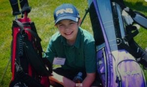 Boy kneeling down on grass between two golf bags.
