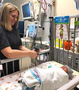 Doctor stands by a NICU bed with a baby in it and places a webcam so the family can see their child when they are away from bedside. 
