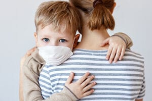 Little boy in medical mask hugging crop mother and looking at camera during coronavirus outbreak 