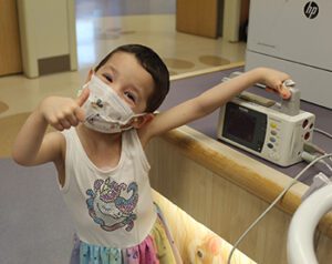 Little girl gives a thumbs up as she carries her wreless monitor that allows her to leave her hospital room