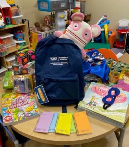 Backpack on a table surrounded by items that will be put inside for siblings of pediatric patients.