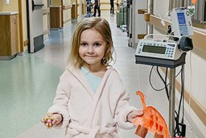 Pediatric patient stands in hospital corridor in her pink robe.