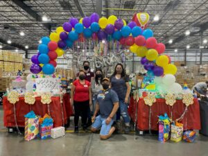 People posing uner a colorful balloon arch in a Costco depot.