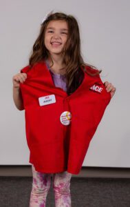 Female pediatric patient poses wearing an Ace Hardware vest and nametag.