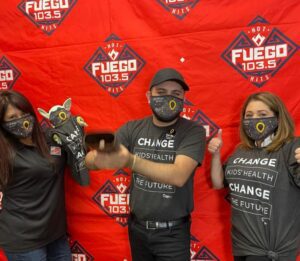 Thre people in masks pose in front of a Fuego banner.