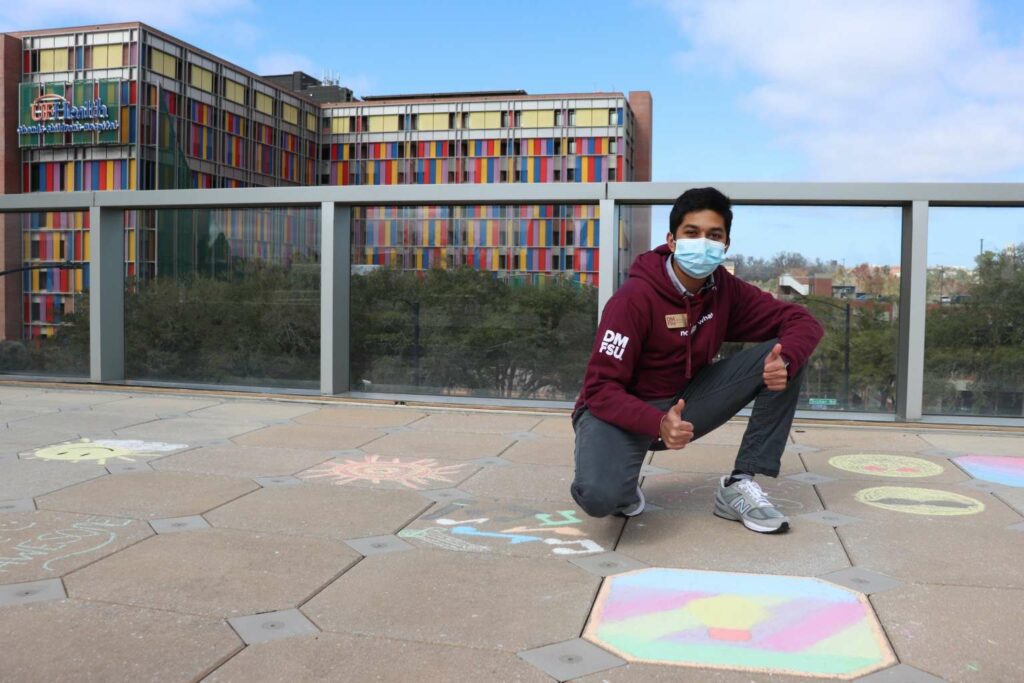 A Dance Marathon at FSU student poses in front of his chalk drawing and the UF Health Shands Children's Hospital.