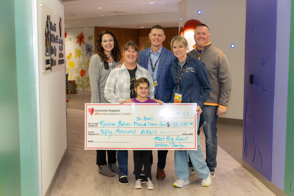 Mia, holding a big check, and her parents stand with Dr. Bock's and his team outside the UH Rainbow Heart Center celebrating her $50,000 donation to the team's research.